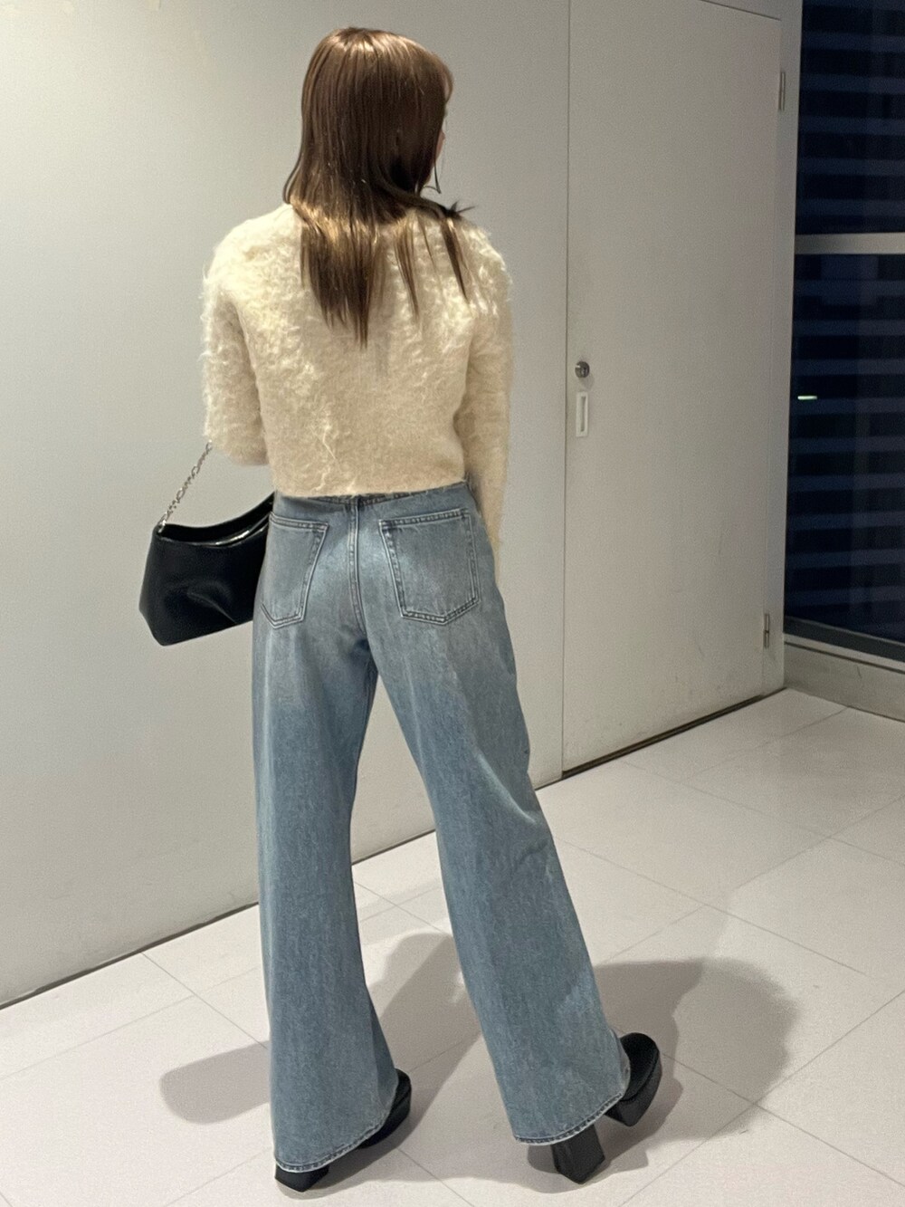 ブルー系のデニムパンツ、ブラック系のハンドバッグ、ホワイト系のニット/セーターを着用したレディースの秋コーディネートの3枚目の写真