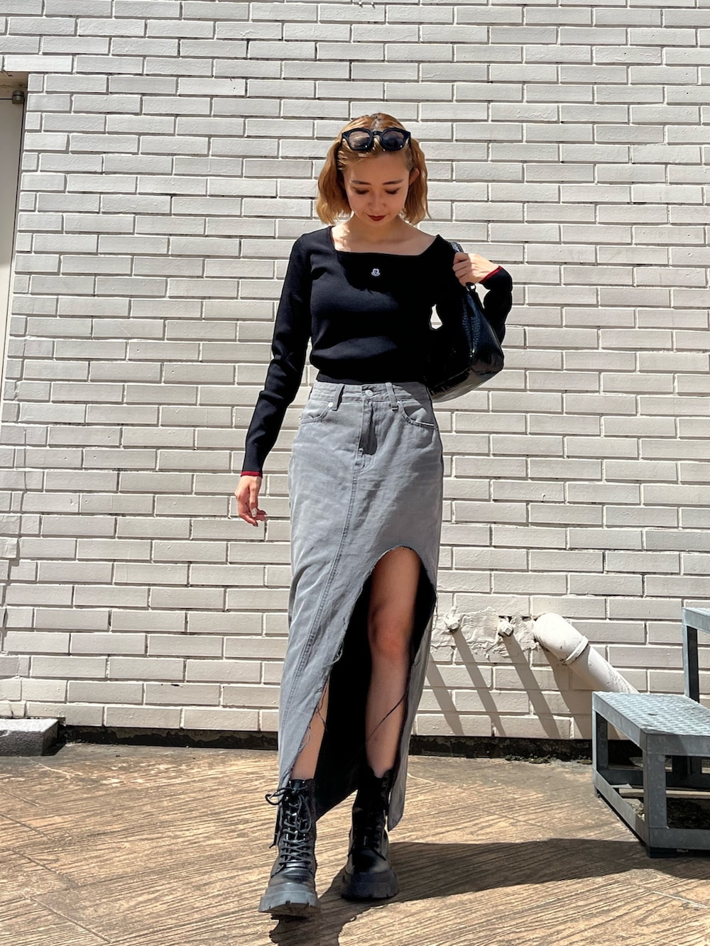 ブラック系のデニムスカート、ブラック系のブーツ、ブラック系のハンドバッグを着用したレディースの夏コーディネートの4枚目の写真