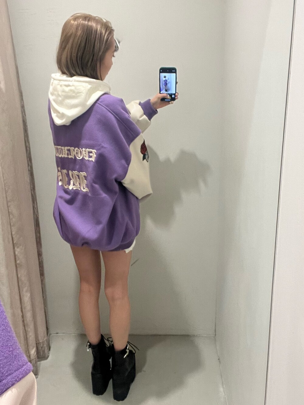 ホワイト系のパーカー、パープル系のスタジャン、ブラック系のブーツを着用したレディースの冬コーディネートの3枚目の写真