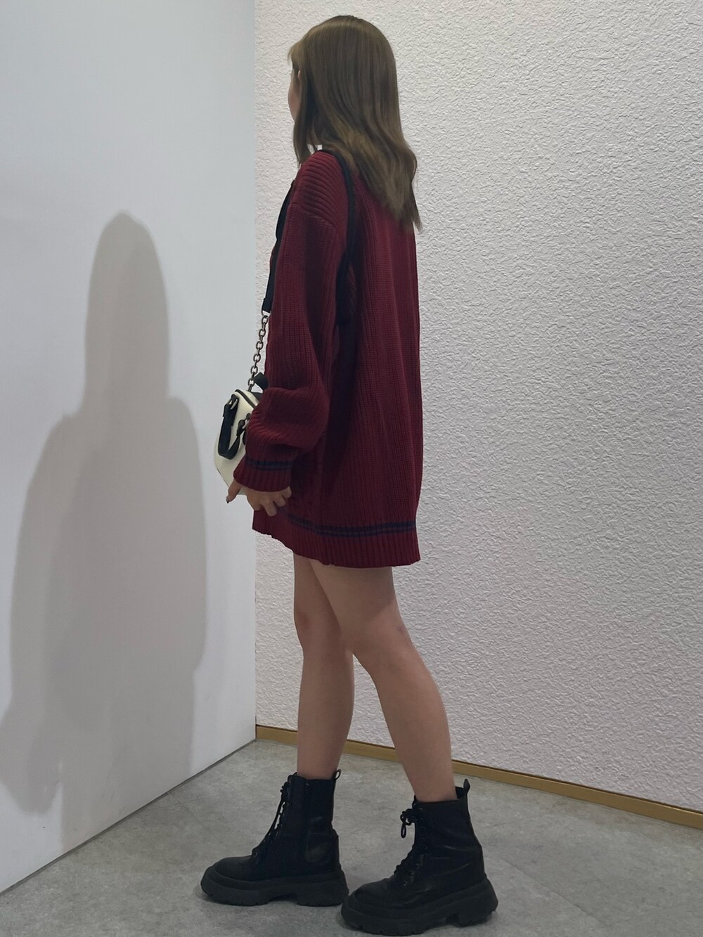 レッド系のニット/セーター、シルバー系のブーツ、ホワイト系のショルダーバッグを着用したレディースの夏コーディネートの2枚目の写真