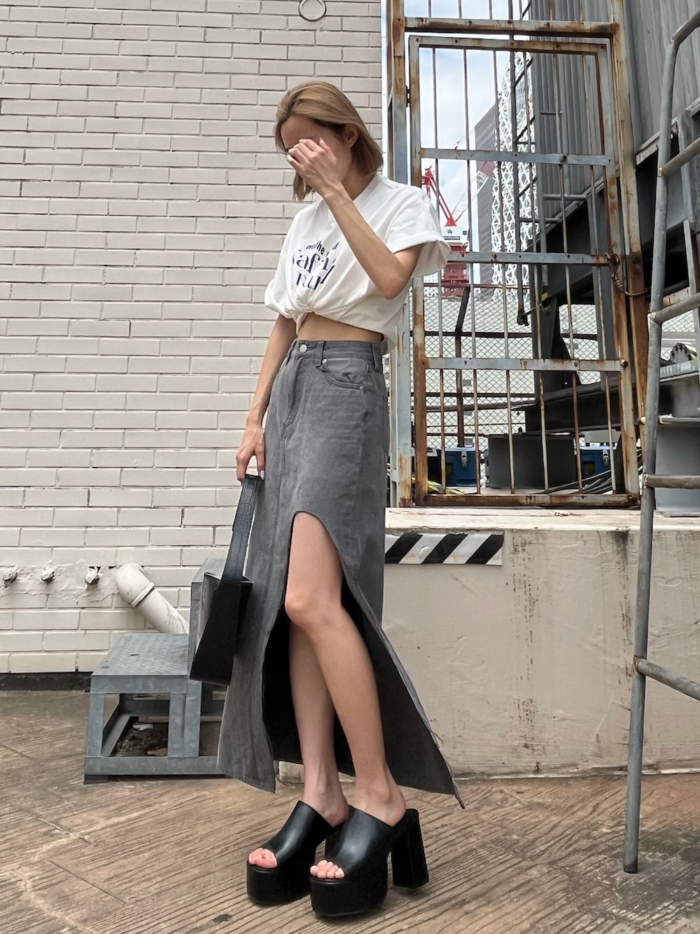 ブラック系のデニムスカート、ブラック系のサンダル、ホワイト系のTシャツ/カットソーを着用したレディースの夏コーディネートの2枚目の写真