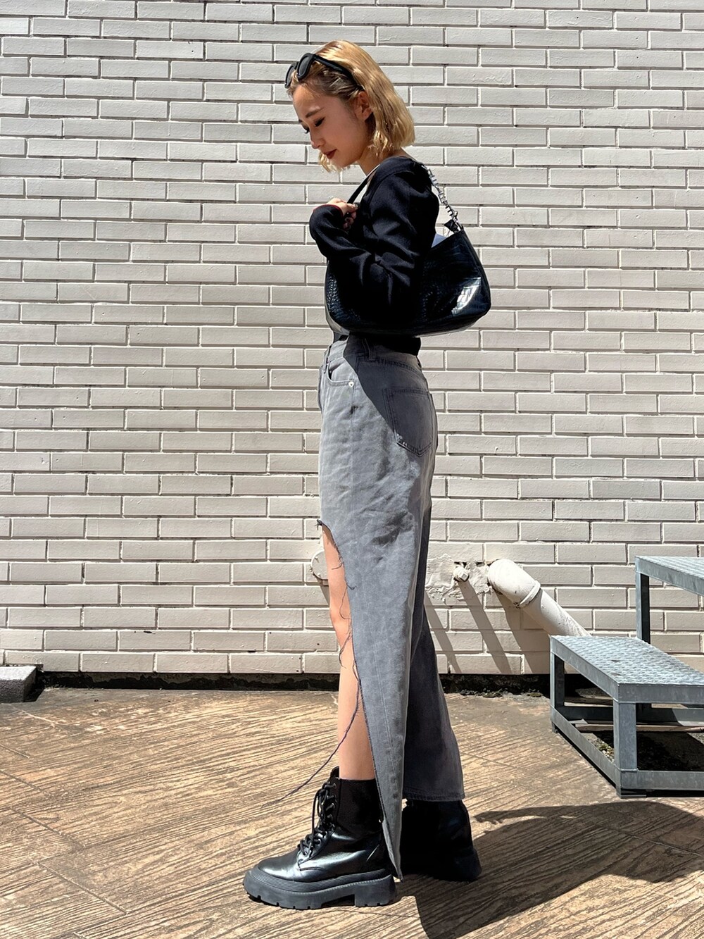 ブラック系のデニムスカート、ブラック系のブーツ、ブラック系のハンドバッグを着用したレディースの夏コーディネートの3枚目の写真