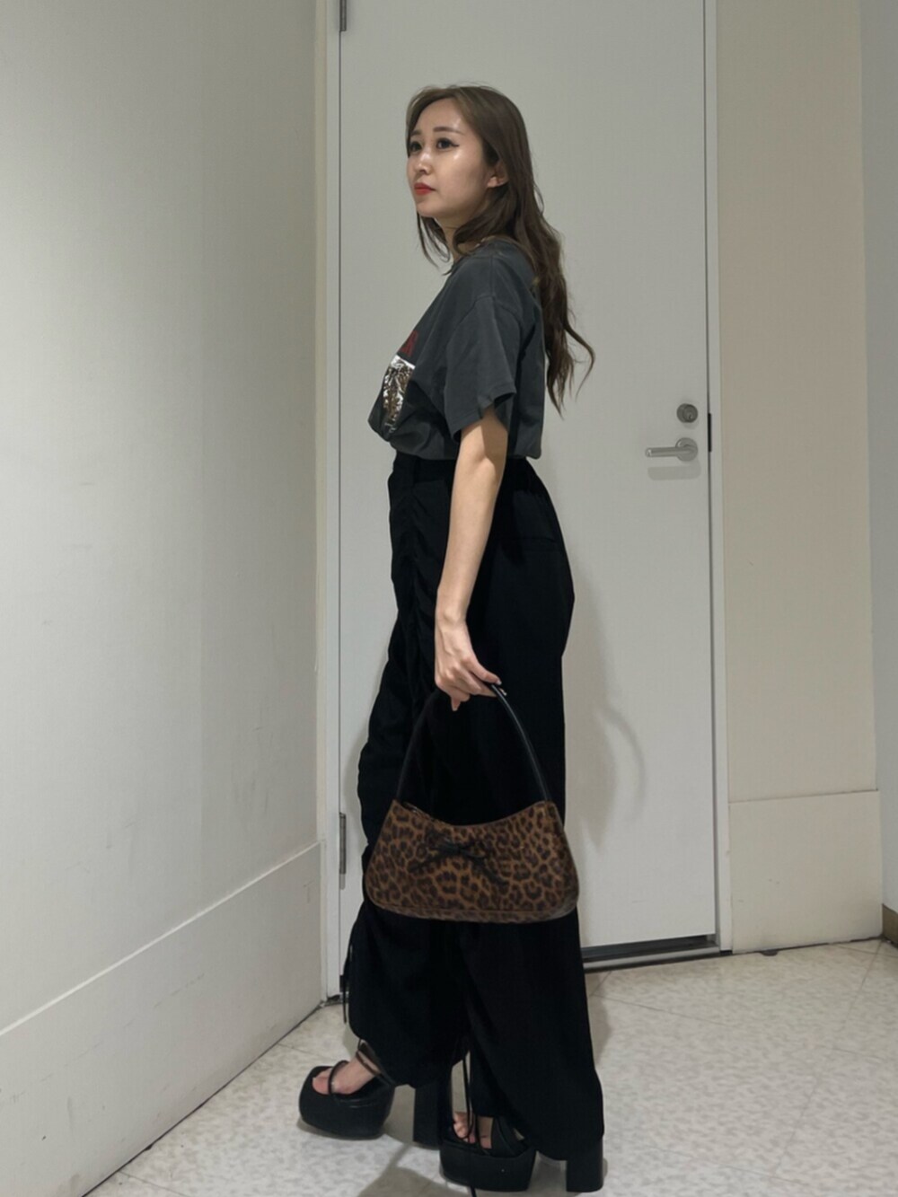 ブラウン系のハンドバッグ、ブラック系のサンダル、ブラック系のTシャツ/カットソーを着用したレディースの夏コーディネートの2枚目の写真