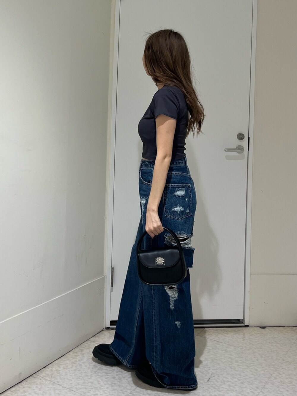 ブラック系のブーツ、ブルー系のデニムパンツ、ブラック系のハンドバッグを着用したレディースの春コーディネートの2枚目の写真