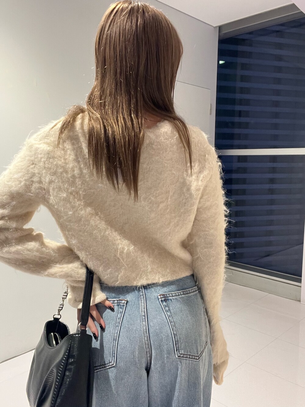 ブルー系のデニムパンツ、ブラック系のハンドバッグ、ホワイト系のニット/セーターを着用したレディースの秋コーディネートの5枚目の写真