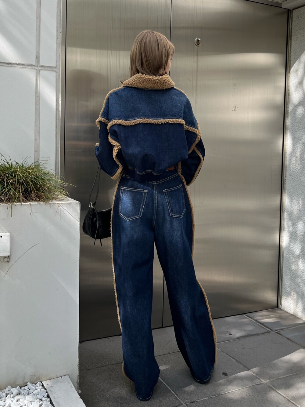 ブラック系のショルダーバッグ、ブラック系のブーツ、ブルー系のデニムパンツを着用したレディースの秋コーディネートの4枚目の写真