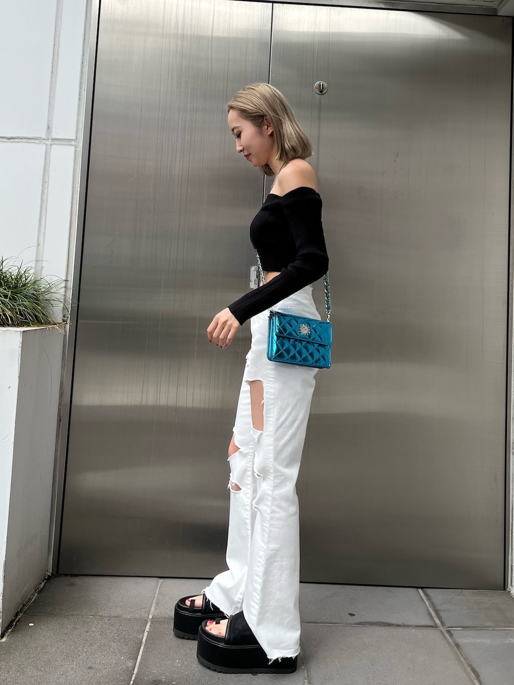 グリーン系のニット/セーター、ブラック系のデニムパンツ、ブラック系のショルダーバッグを着用したレディースの春コーディネートの2枚目の写真