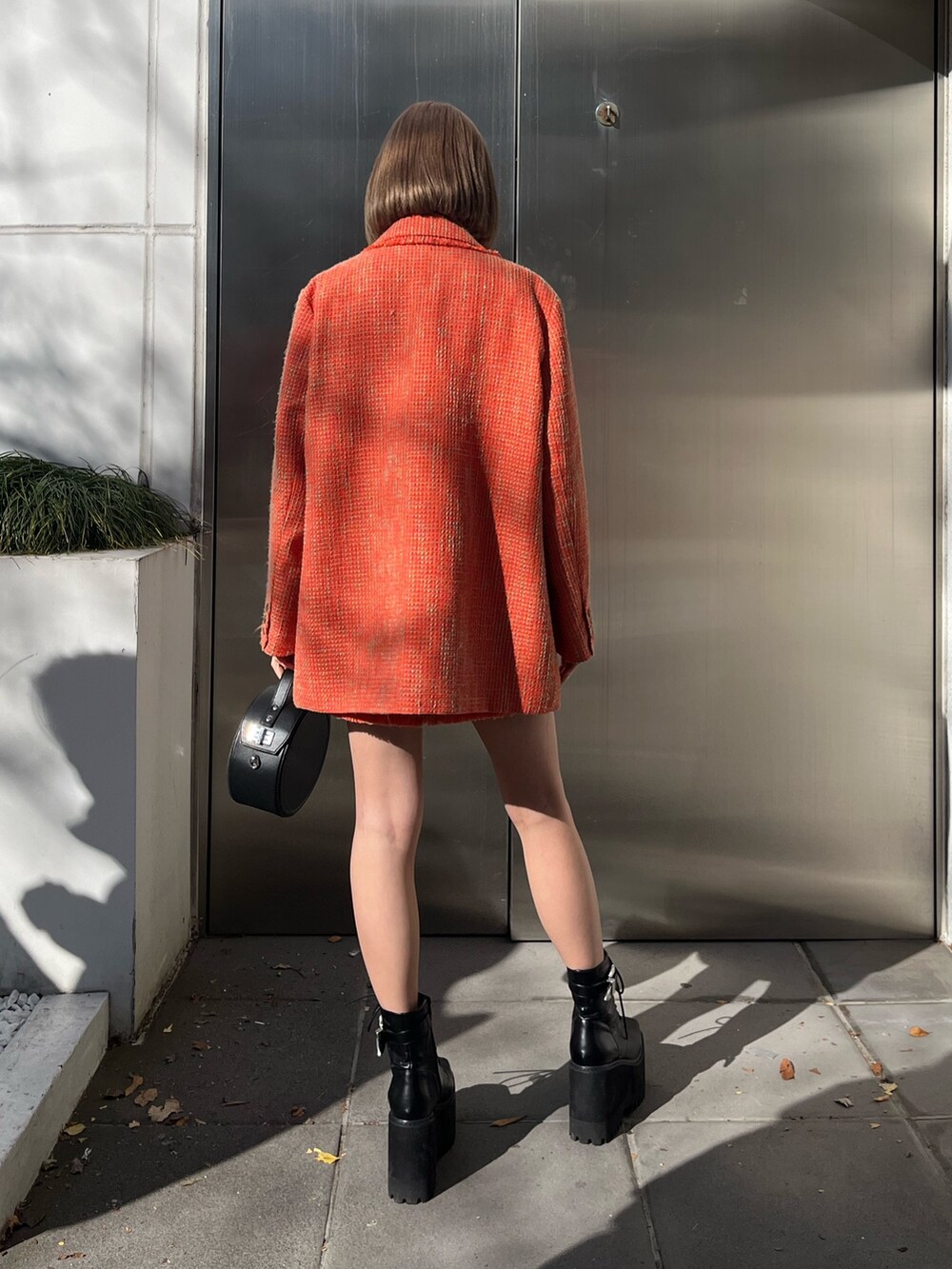 オレンジ系のテーラードジャケット、オレンジ系のキャミソール、ブラック系のブーツを着用したレディースの冬コーディネートの4枚目の写真