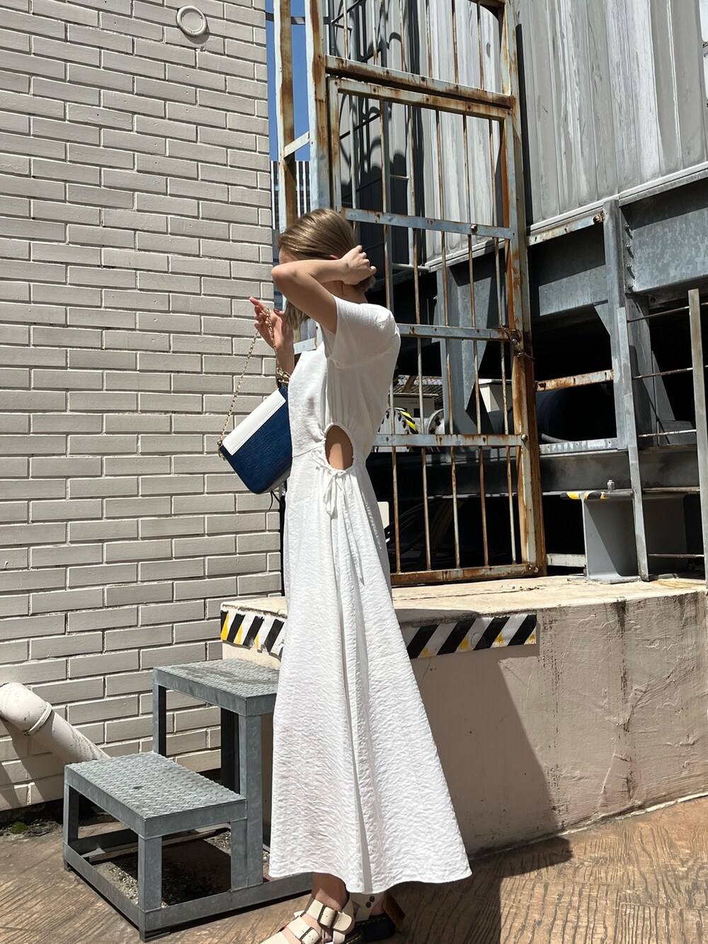 ホワイト系のワンピース、ベージュ系のサンダル、ブルー系のショルダーバッグを着用したレディースの春コーディネートの2枚目の写真