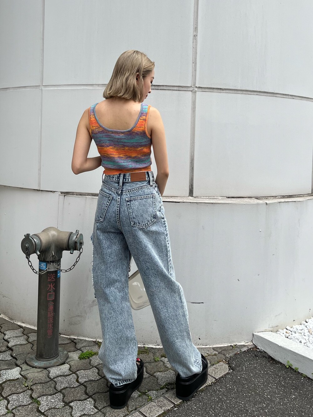 ブルー系のデニムパンツ、オレンジ系のタンクトップ、ブラック系のサンダルを着用したレディースの春コーディネートの3枚目の写真