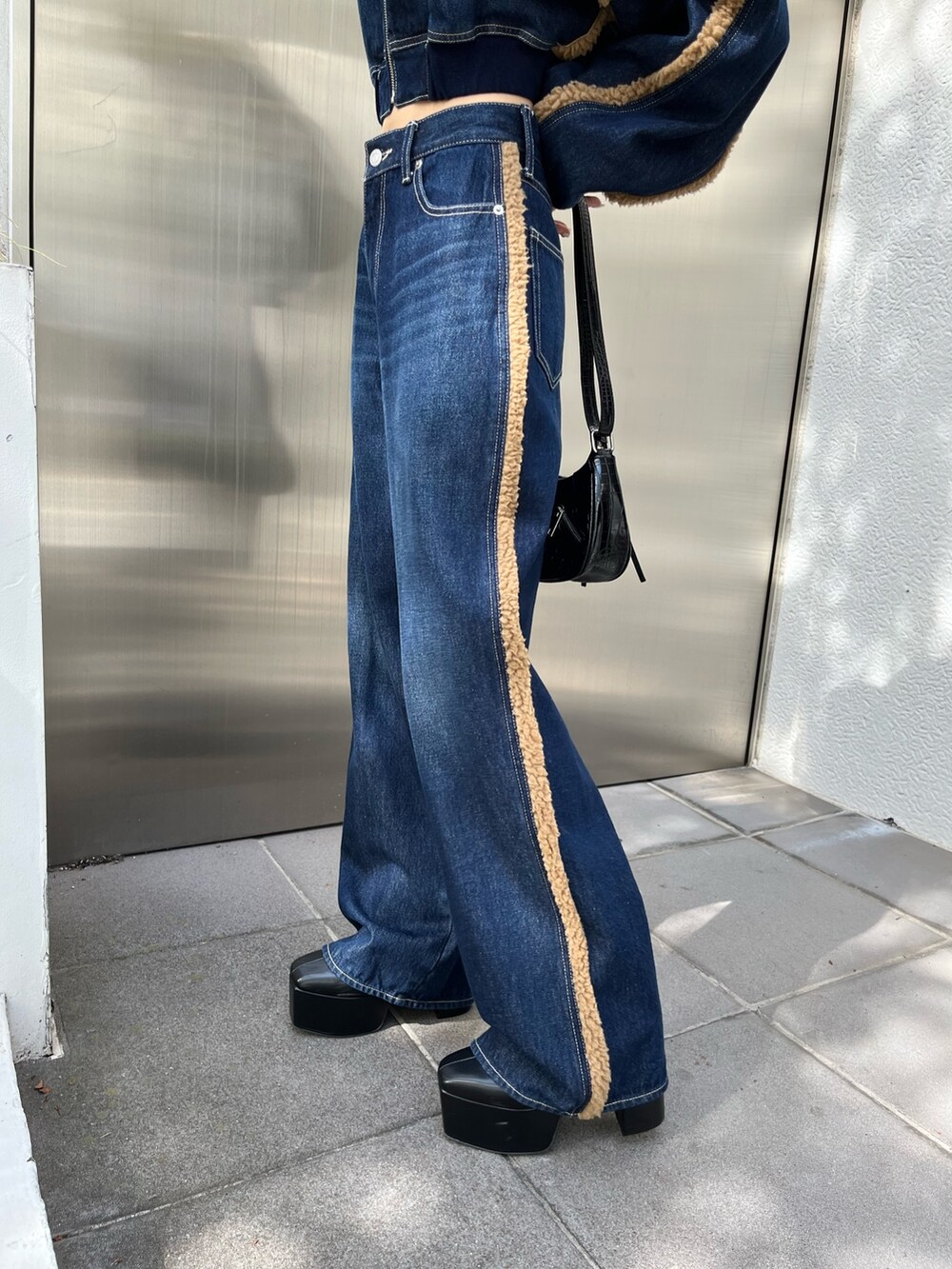 ブラック系のショルダーバッグ、ブラック系のブーツ、ブルー系のデニムパンツを着用したレディースの秋コーディネートの8枚目の写真