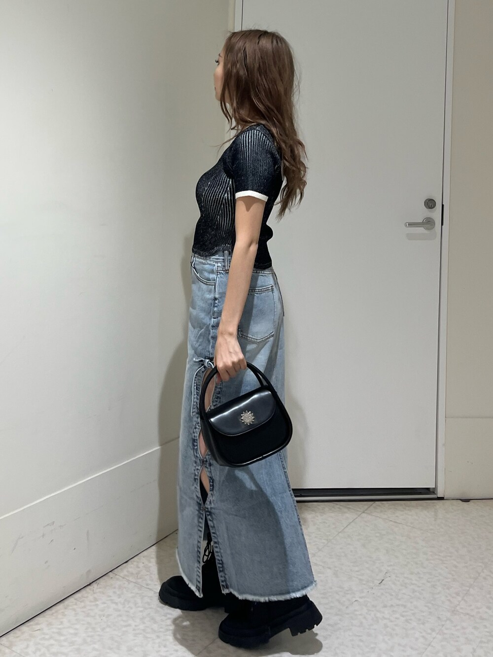 ブラック系のブーツ、ブルー系のデニムスカート、ブラック系のハンドバッグを着用したレディースの春コーディネートの2枚目の写真
