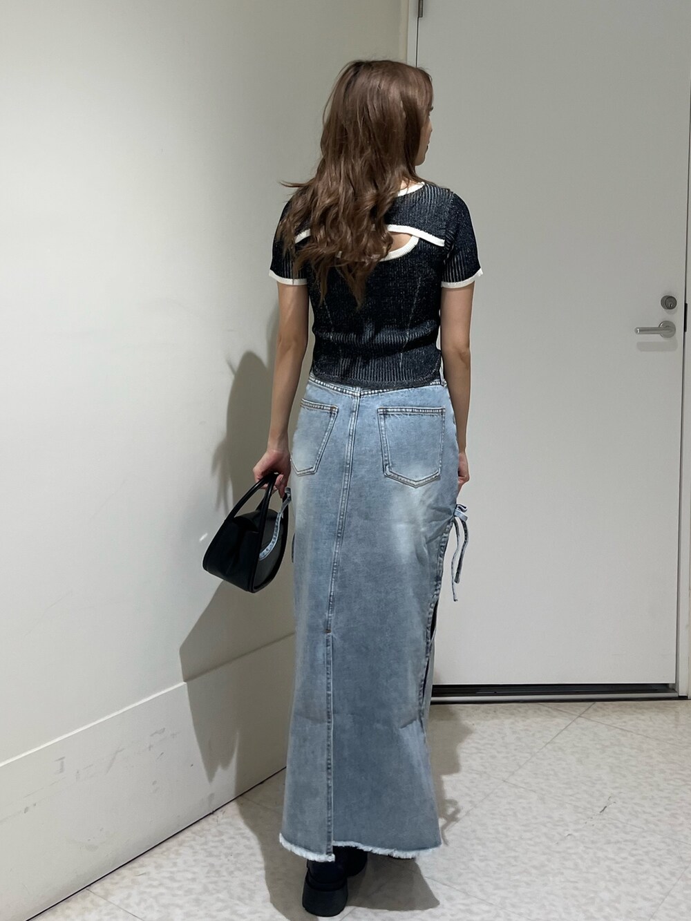 ブラック系のブーツ、ブルー系のデニムスカート、ブラック系のハンドバッグを着用したレディースの春コーディネートの3枚目の写真