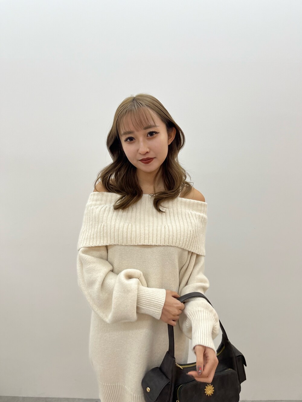 グレー系のハンドバッグ、ホワイト系のワンピース、ブラック系のブーツを着用したレディースの冬コーディネートの4枚目の写真