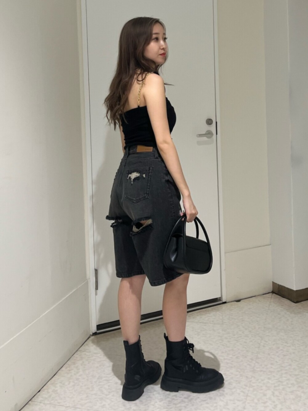 ブラック系のブーツ、ブラック系のハンドバッグ、ブラック系のデニムパンツを着用したレディースの夏コーディネートの2枚目の写真