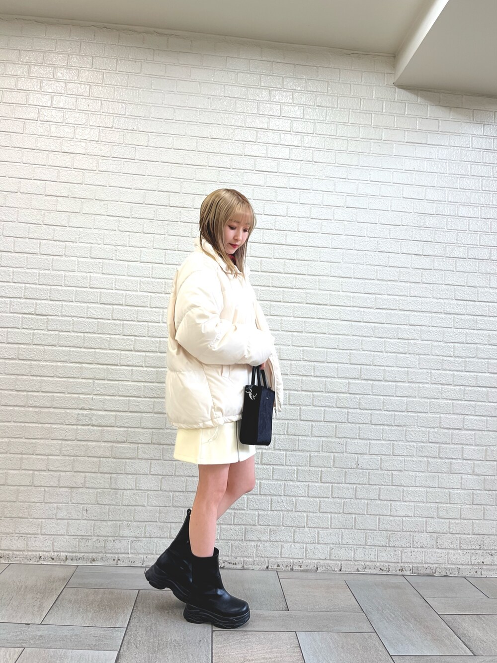 ブラック系のブーツ、ホワイト系のダウンジャケット/コート、ブラック系のショルダーバッグを着用したレディースの冬コーディネートの2枚目の写真