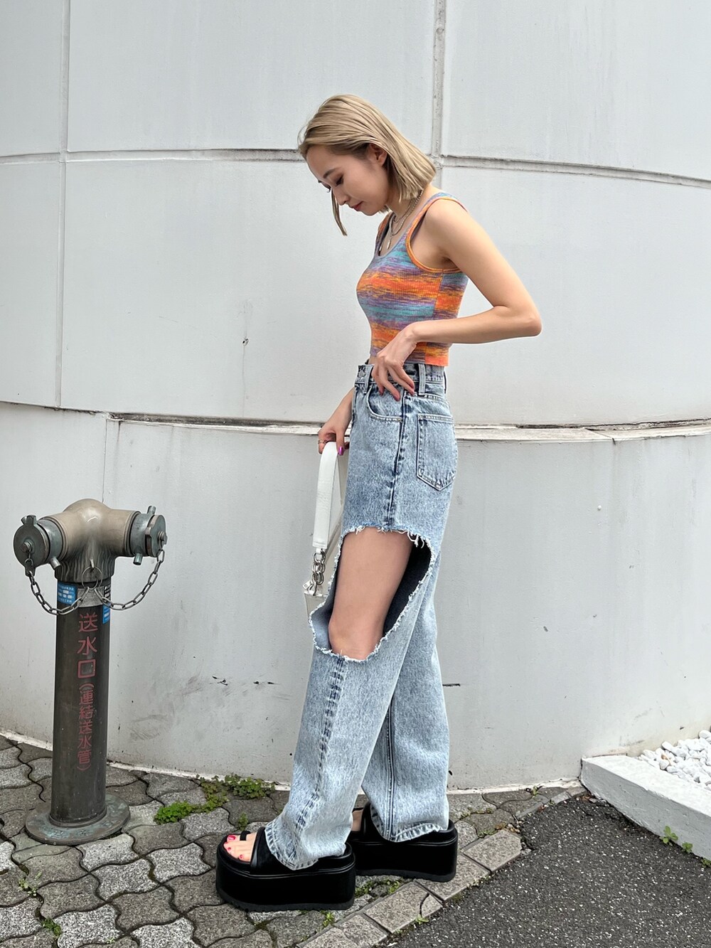 ブルー系のデニムパンツ、オレンジ系のタンクトップ、ブラック系のサンダルを着用したレディースの春コーディネートの2枚目の写真