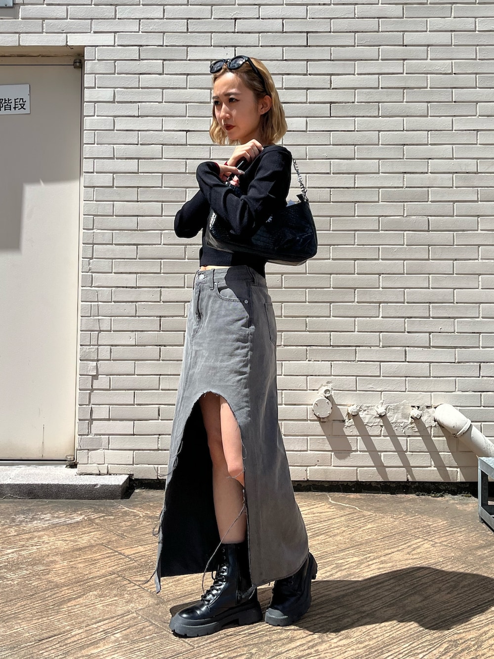 ブラック系のデニムスカート、ブラック系のブーツ、ブラック系のハンドバッグを着用したレディースの夏コーディネートの2枚目の写真