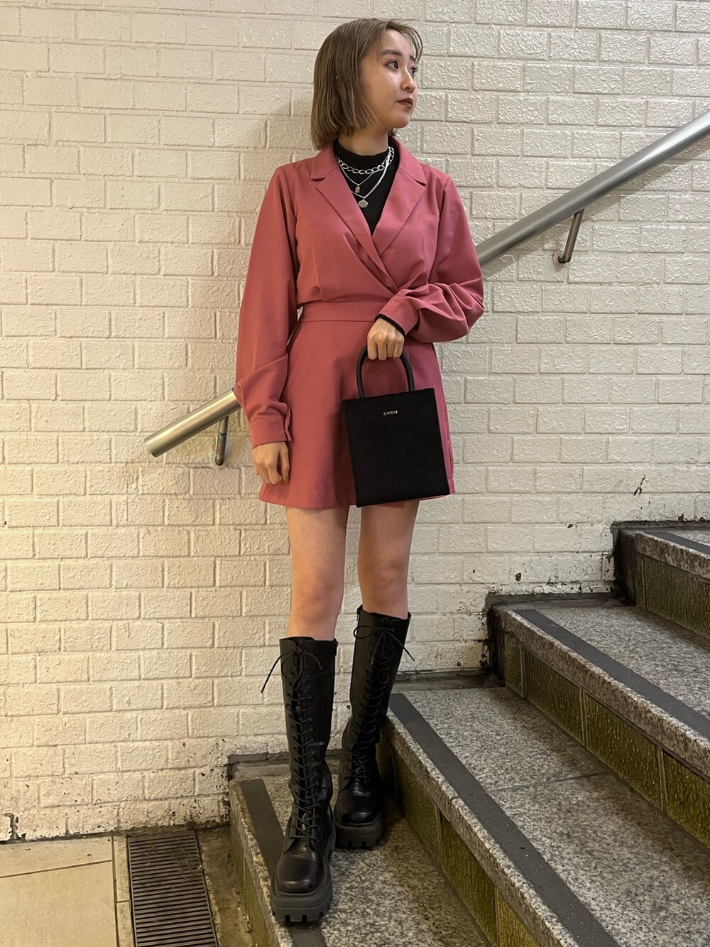 ブラック系のブーツ、ブラック系のショルダーバッグ、ピンク系のワンピースを着用したレディースの冬コーディネートの2枚目の写真