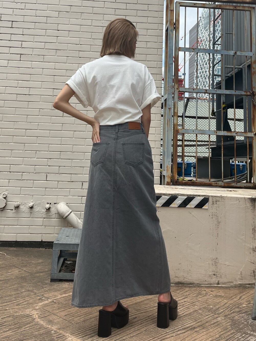 ブラック系のデニムスカート、ブラック系のサンダル、ホワイト系のTシャツ/カットソーを着用したレディースの夏コーディネートの4枚目の写真