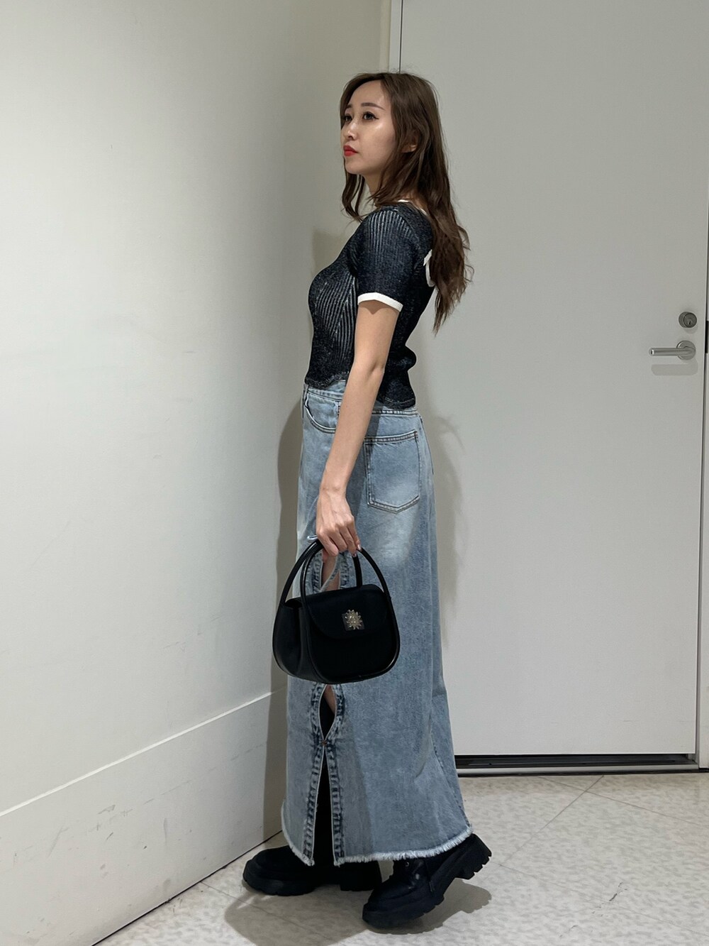 ブラック系のブーツ、ブルー系のデニムスカート、ブラック系のハンドバッグを着用したレディースの春コーディネートの4枚目の写真