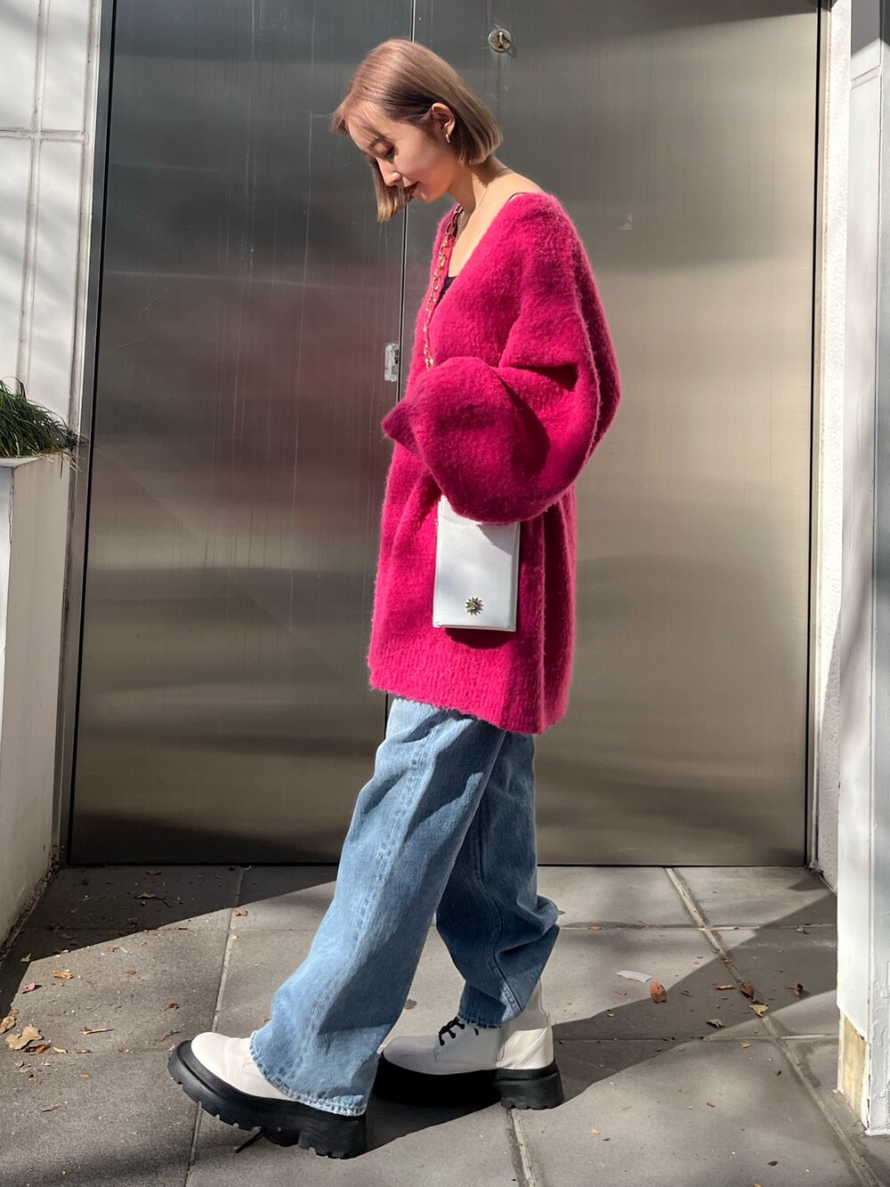 ブルー系のデニムパンツ、ホワイト系のショルダーバッグ、ピンク系のカーディガン/ボレロを着用したレディースの冬コーディネートの2枚目の写真