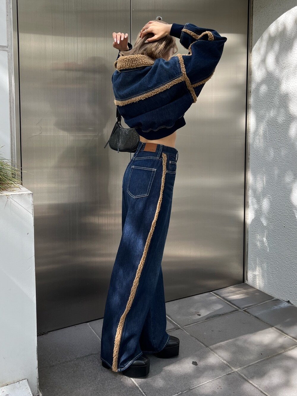 ブラック系のショルダーバッグ、ブラック系のブーツ、ブルー系のデニムパンツを着用したレディースの秋コーディネートの5枚目の写真