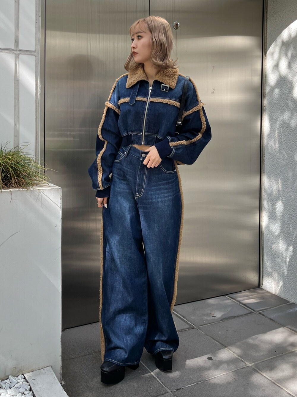 ブラック系のショルダーバッグ、ブラック系のブーツ、ブルー系のデニムパンツを着用したレディースの秋コーディネートの3枚目の写真