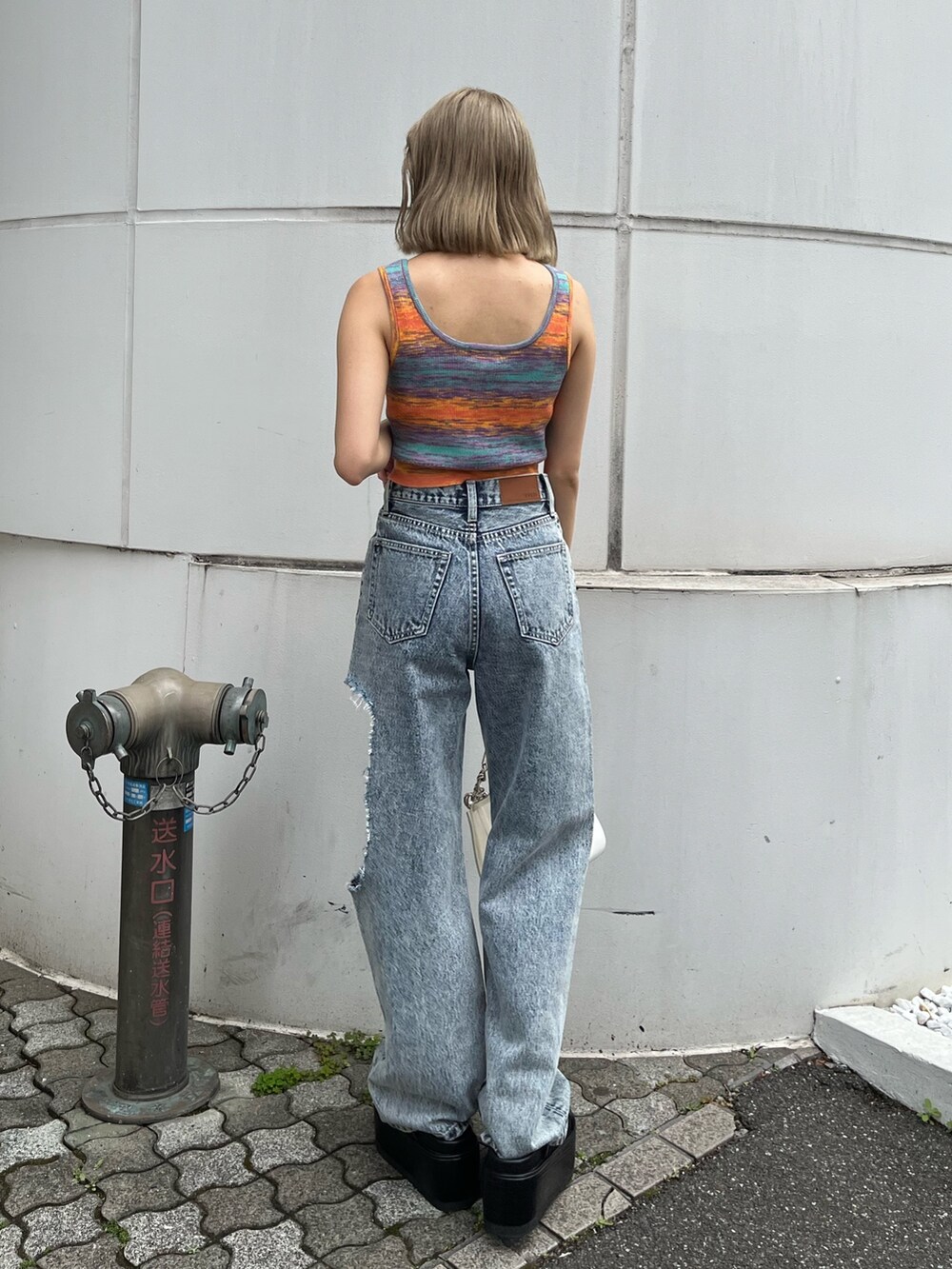 ブルー系のデニムパンツ、オレンジ系のタンクトップ、ブラック系のサンダルを着用したレディースの春コーディネートの4枚目の写真