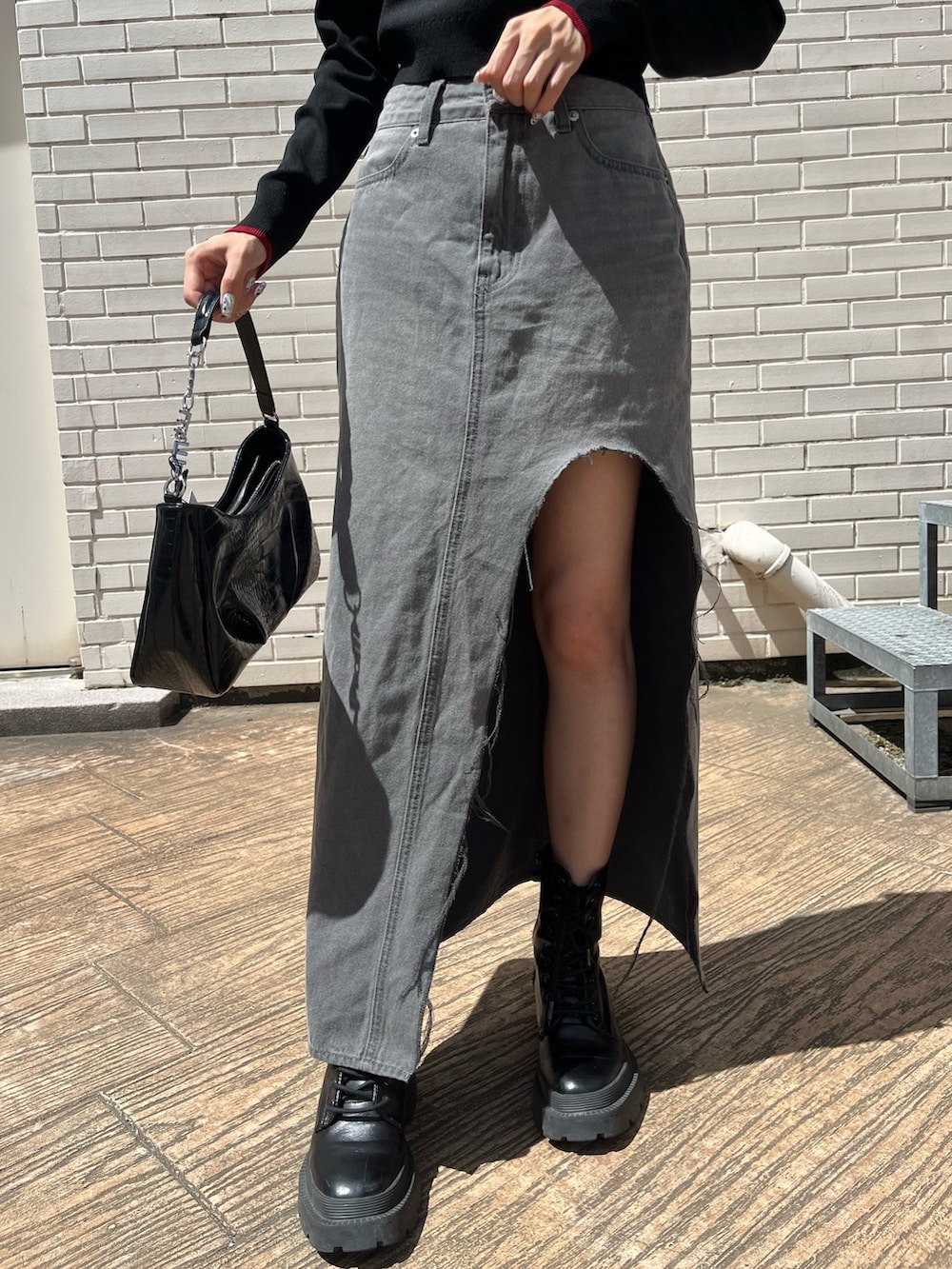 ブラック系のデニムスカート、ブラック系のブーツ、ブラック系のハンドバッグを着用したレディースの夏コーディネートの6枚目の写真