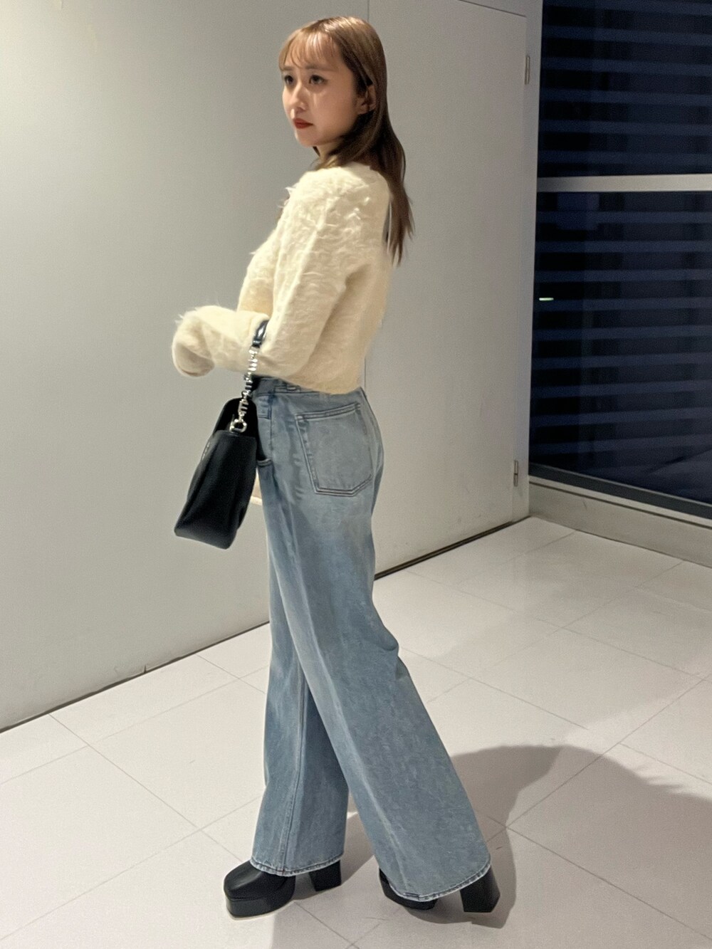 ブルー系のデニムパンツ、ブラック系のハンドバッグ、ホワイト系のニット/セーターを着用したレディースの秋コーディネートの2枚目の写真