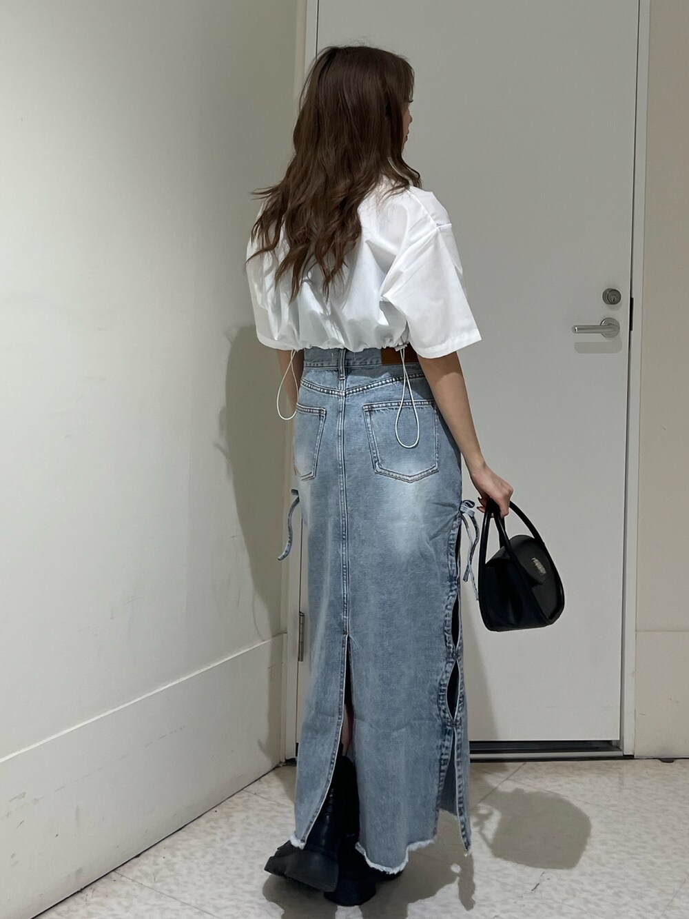 ブラック系のブーツ、ブルー系のデニムスカート、ブラック系のハンドバッグを着用したレディースの春コーディネートの3枚目の写真