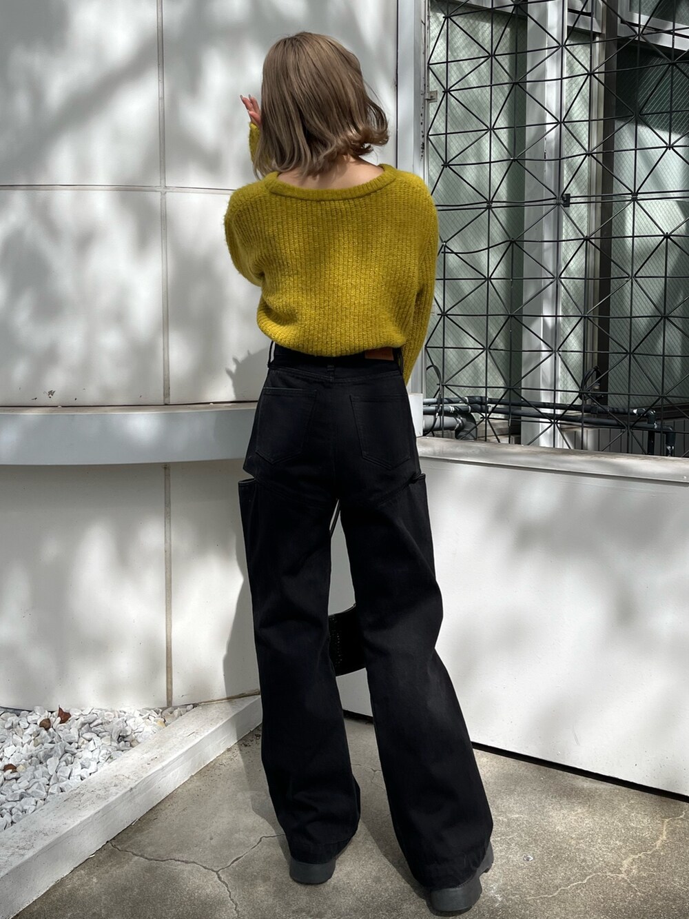 ブラック系のショルダーバッグ、ブラック系のデニムパンツ、イエロー系のニット/セーターを着用したレディースの秋コーディネートの4枚目の写真