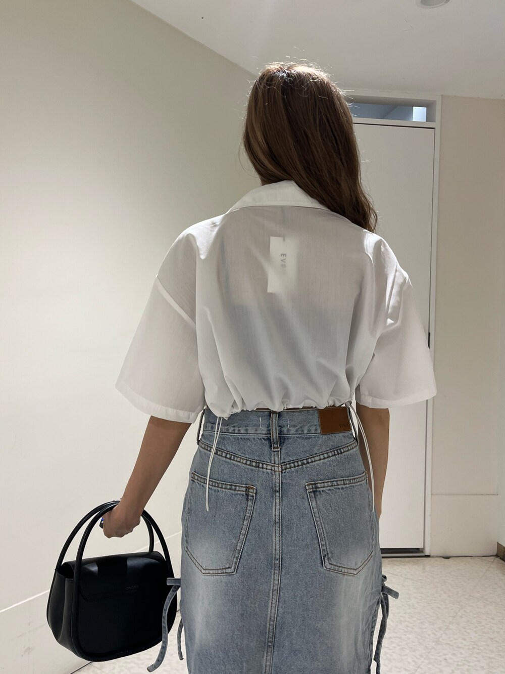 ブラック系のブーツ、ブルー系のデニムスカート、ブラック系のハンドバッグを着用したレディースの春コーディネートの6枚目の写真