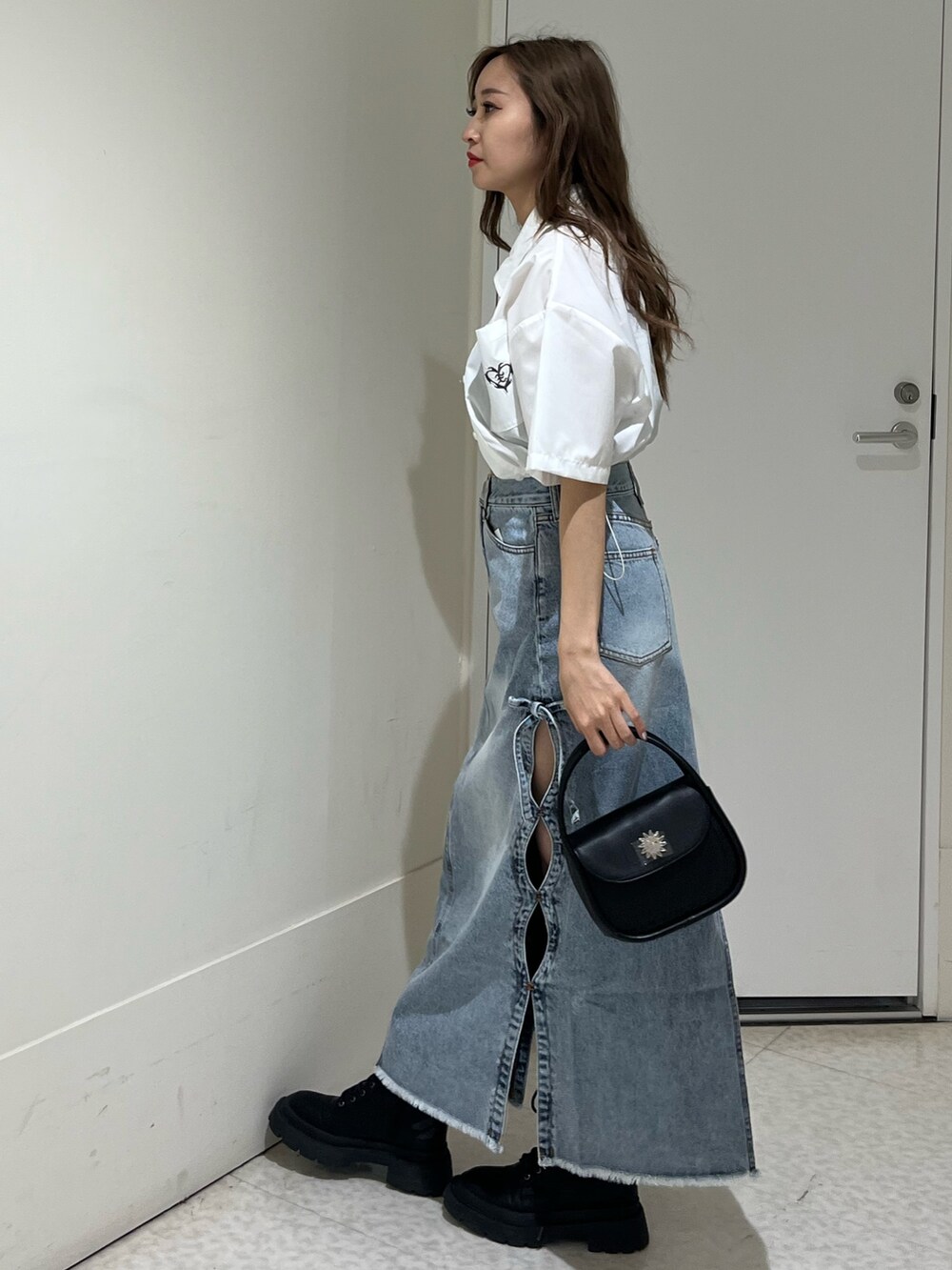 ブラック系のブーツ、ブルー系のデニムスカート、ブラック系のハンドバッグを着用したレディースの春コーディネートの2枚目の写真