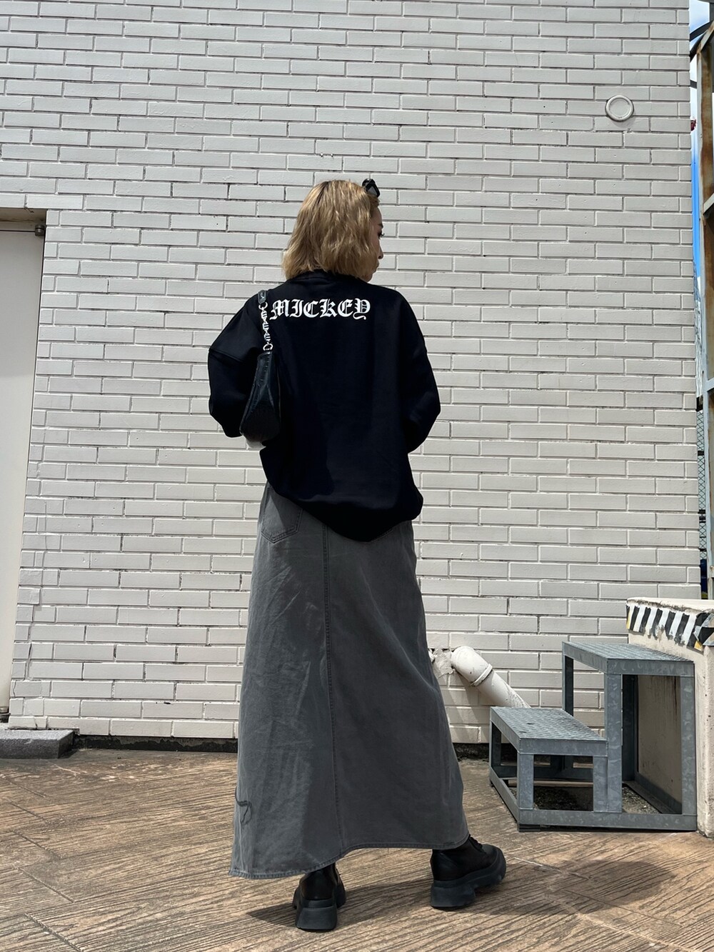 ブラック系のデニムスカート、ホワイト系のブーツ、ブラック系のハンドバッグを着用したレディースの夏コーディネートの3枚目の写真