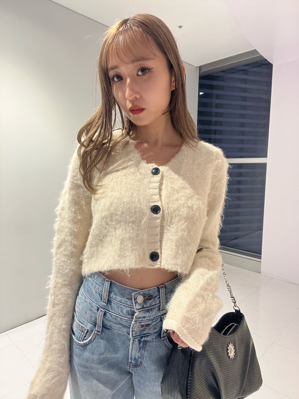 ブルー系のデニムパンツ、ブラック系のハンドバッグ、ホワイト系のニット/セーターを着用したレディースの秋コーディネートの4枚目の写真