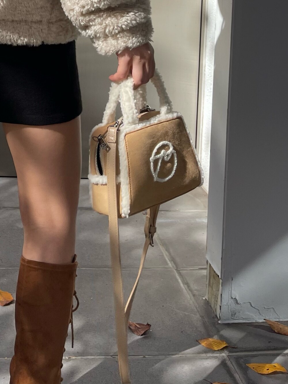 ホワイト系のブルゾン、ベージュ系のハンドバッグ、ブラウン系のブーツを着用したレディースの冬コーディネートの6枚目の写真