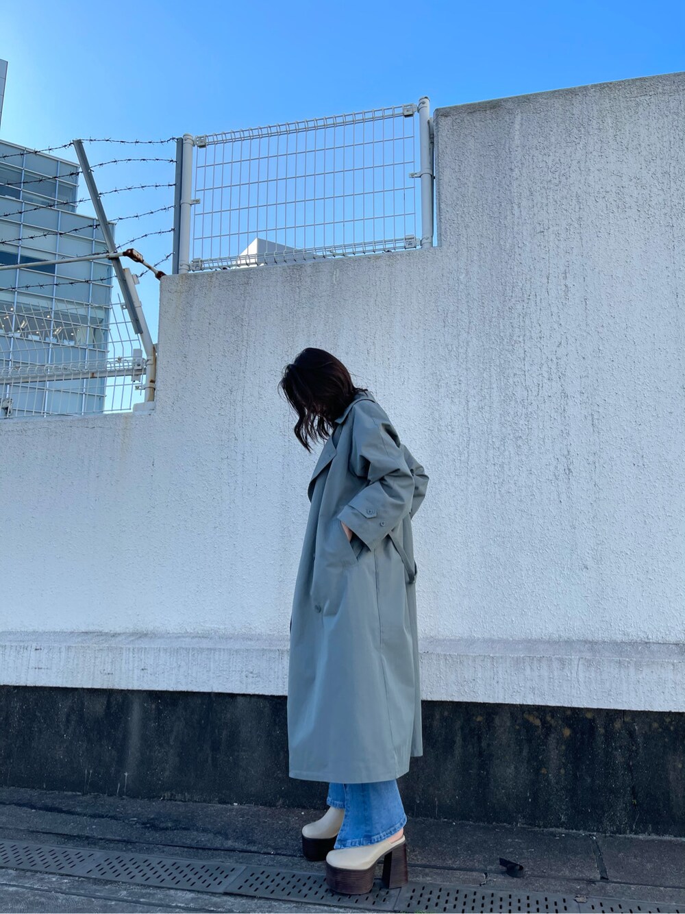 グリーン系のトレンチコート、ホワイト系のサンダル、ブルー系のデニムパンツを着用したレディースの冬コーディネートの7枚目の写真