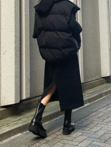 ブラック系のダウンベスト、ブラック系のワンピース、ブラック系のブーツを着用したレディースの秋コーディネートの6枚目の写真