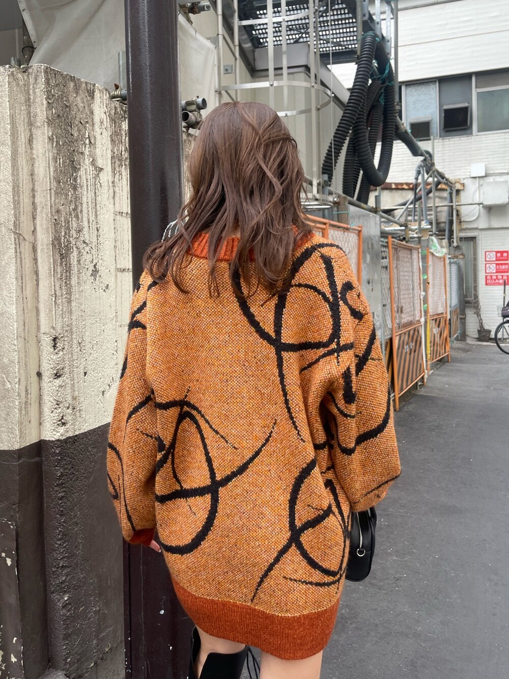 オレンジ系のニット/セーター、ブラック系のハンドバッグ、ブラック系のブーツを着用したレディースの秋コーディネートの6枚目の写真