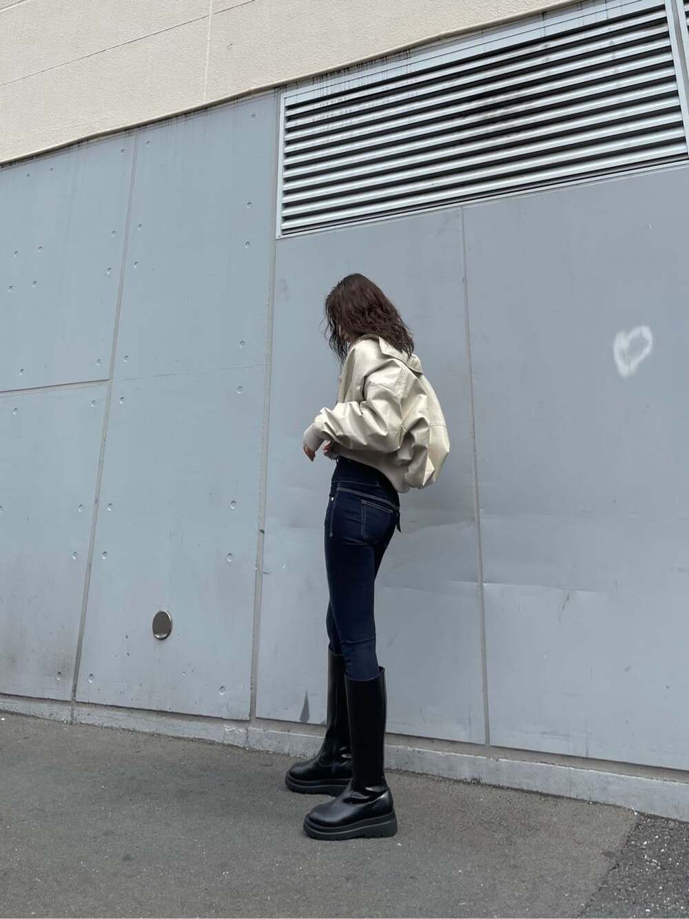 ホワイト系のブルゾン、ブラック系のブーツ、ブルー系のデニムパンツを着用したレディースの秋コーディネートの2枚目の写真