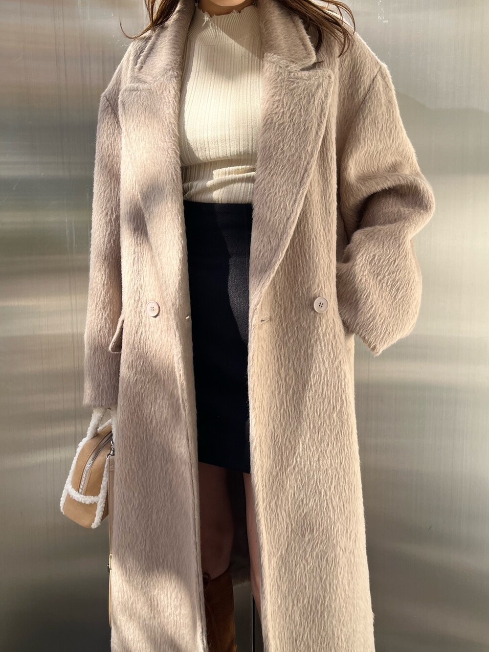 ブラック系のスカート、ベージュ系のハンドバッグ、ブラウン系のブーツを着用したレディースの秋コーディネートの4枚目の写真