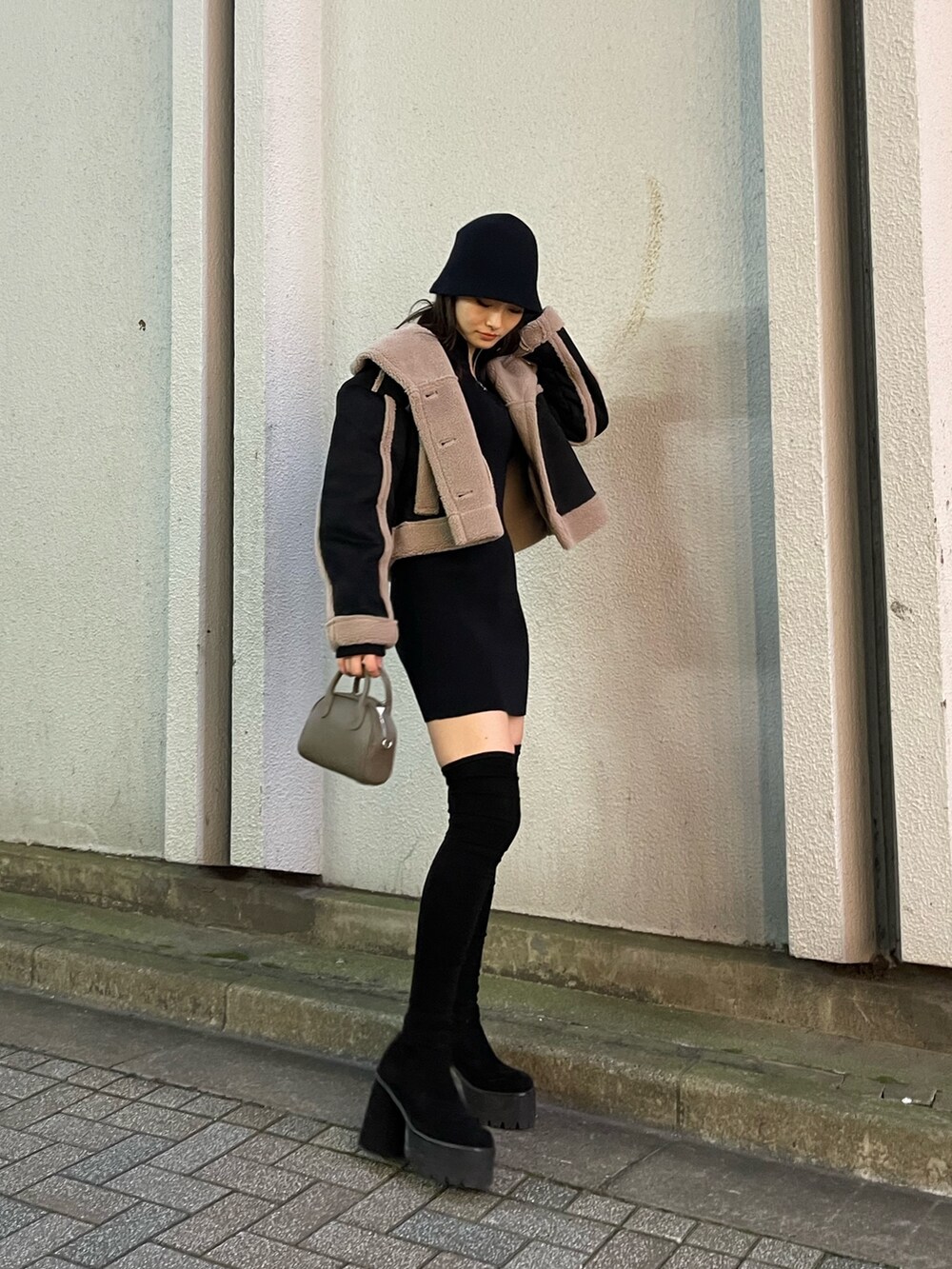 ブラック系のムートンコート、ブラウン系のハンドバッグ、ブラック系のブーツを着用したレディースの秋コーディネートの3枚目の写真