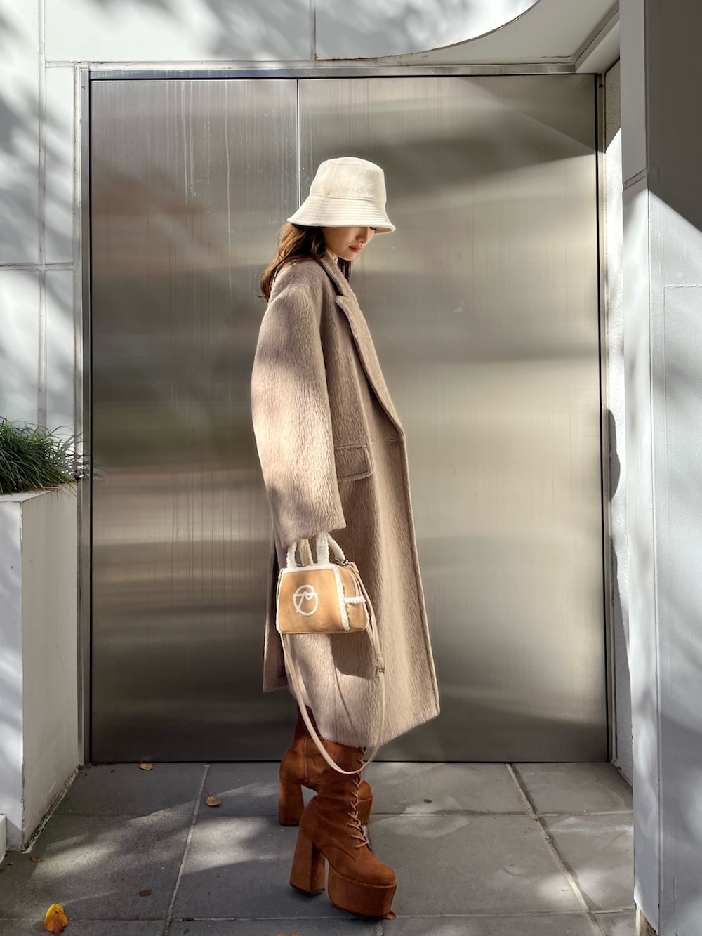 ブラック系のスカート、ベージュ系のハンドバッグ、ブラウン系のブーツを着用したレディースの秋コーディネートの2枚目の写真