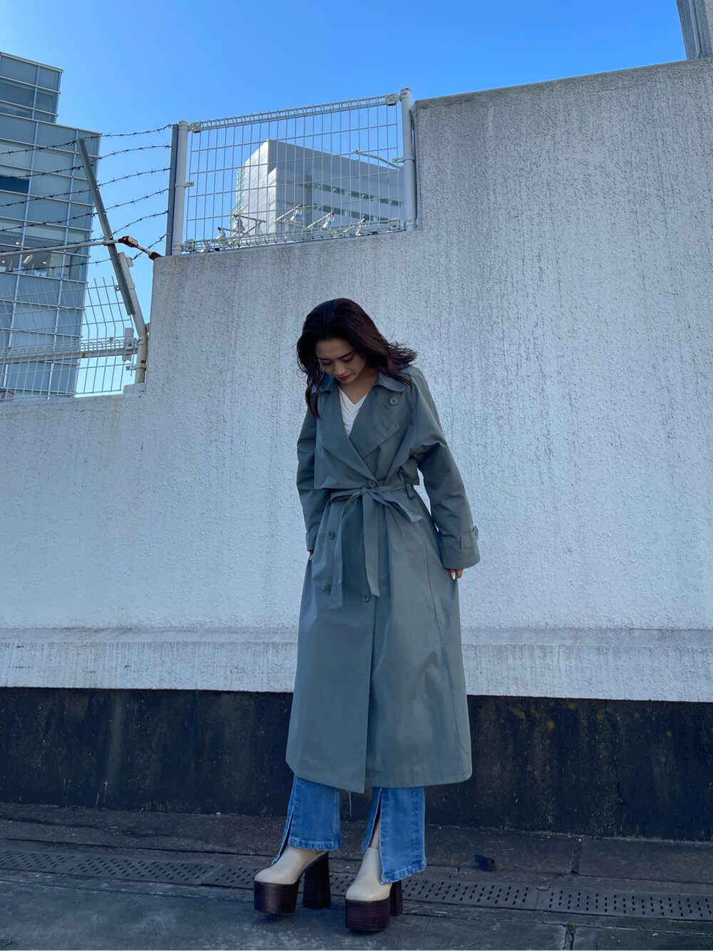 グリーン系のトレンチコート、ホワイト系のサンダル、ブルー系のデニムパンツを着用したレディースの冬コーディネートの6枚目の写真
