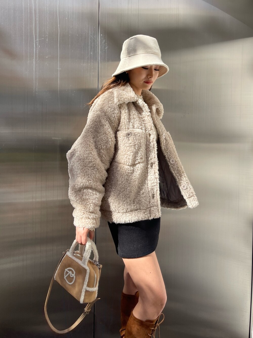 ホワイト系のブルゾン、ベージュ系のハンドバッグ、ブラウン系のブーツを着用したレディースの冬コーディネートの3枚目の写真