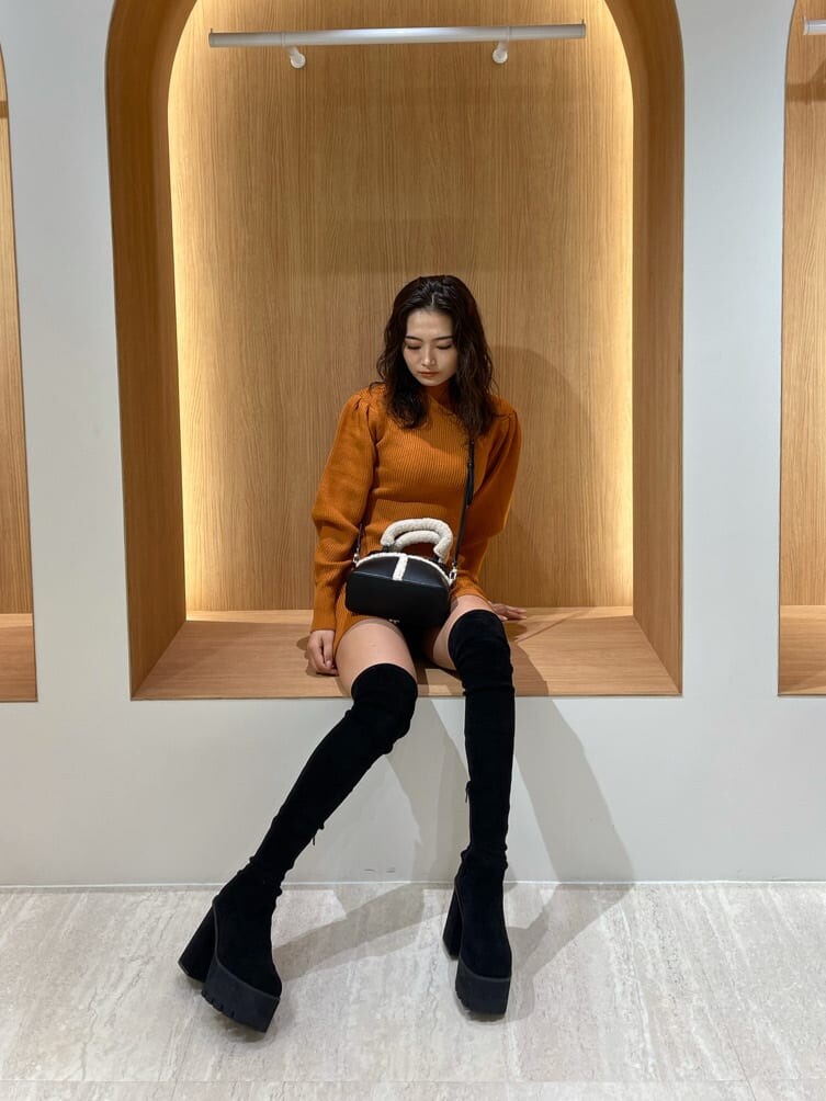 オレンジ系のワンピース、ブラック系のブーツ、ブラック系のハンドバッグを着用したレディースの秋コーディネートの2枚目の写真