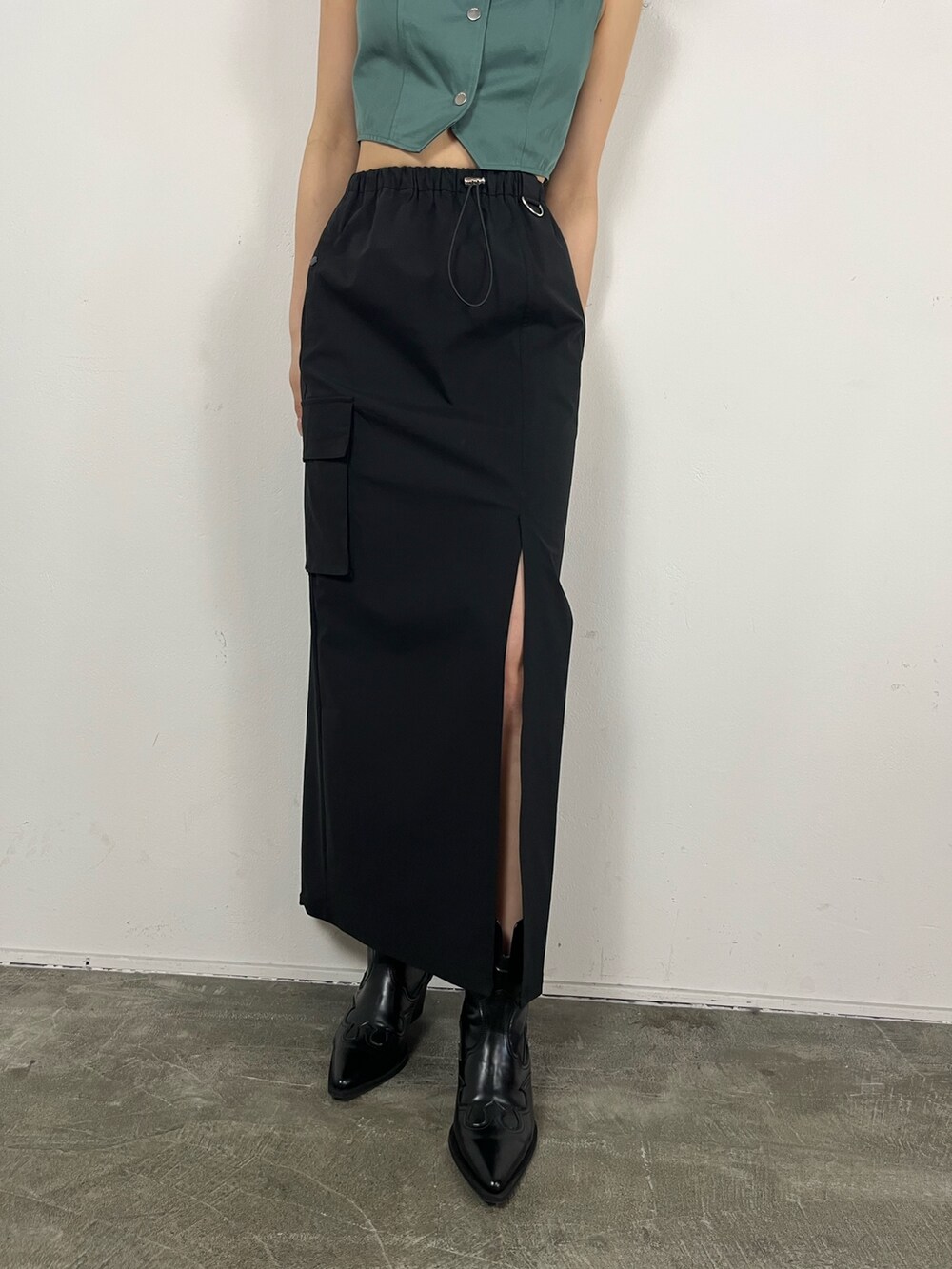 ブラック系のスカート、グリーン系のキャミソール、ブラック系のブーツを着用したレディースの春コーディネートの6枚目の写真