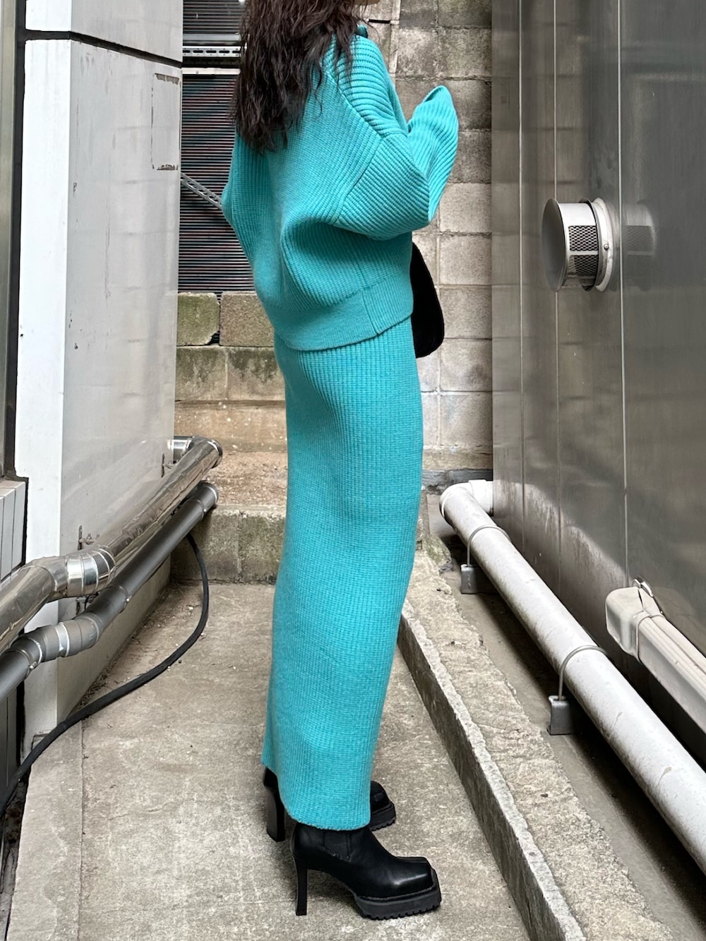 ブラック系のハンドバッグ、ブラック系のブーツ、ブルー系のスカートを着用したレディースの秋コーディネートの3枚目の写真